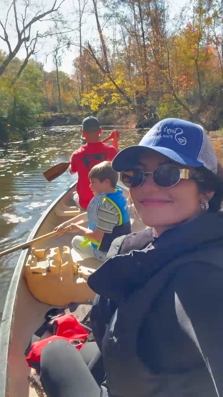 A woman smiling over her shoulder from the stern of a canoe while two boys paddle ahead of her on Bayou Bartholomew